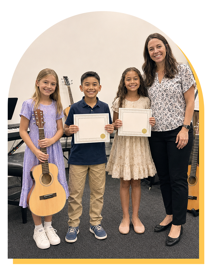 Three smiling children stand with certificates and a guitar, next to an adult woman in a music school setting. Musical instruments in the background suggest they’ve just finished music lessons Citrus Park or an award event in music lessons Tampa.